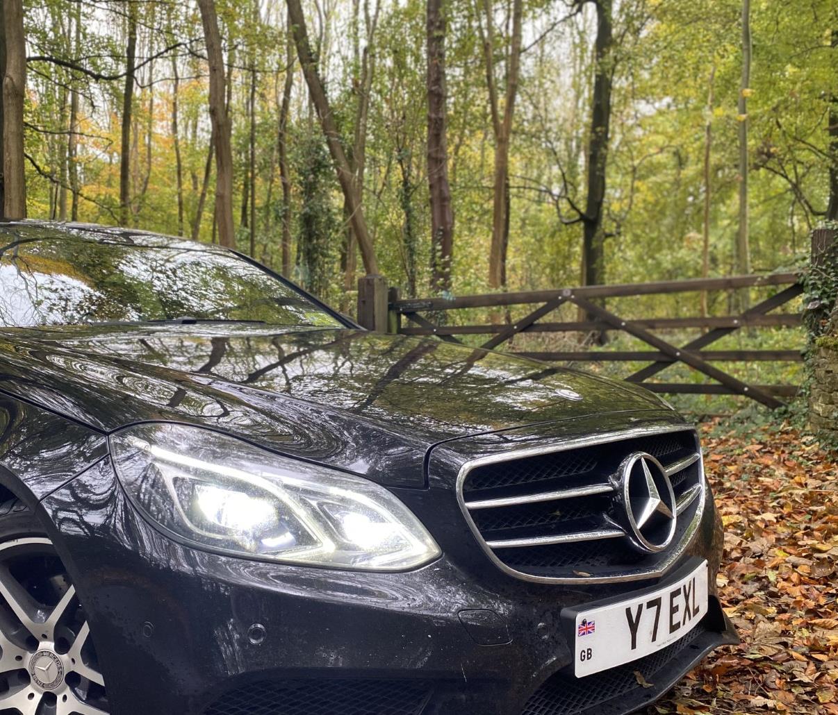 A black Mercedes E-class parked just outside of Kingham village in a wooded location